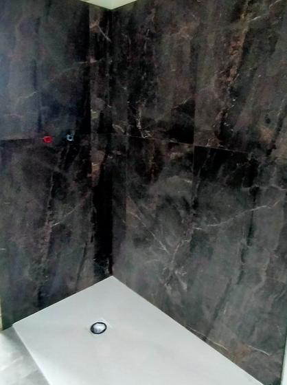 Angolo doccia rivestito con grandi lastre scure venate, piatto doccia bianco con piletta al centro