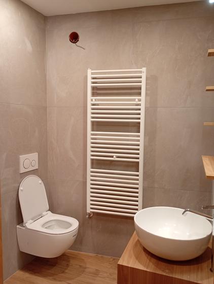 Bagno con rivestimento in gres beige a grande formato, scaldasalviette a parete, top in legno e lavabo a bacinella