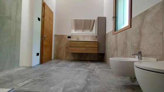 Bagno finito: pavimento grigio venato di grande formato, rivestimento beige, mobile sospeso in legno, sanitari sospesi
