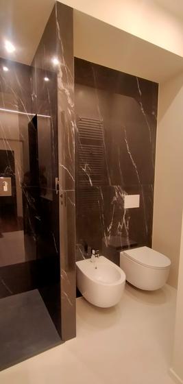 Bagno rivestito in grandi lastre effetto marmo nero venato, con sanitari sospesi e pavimento chiaro