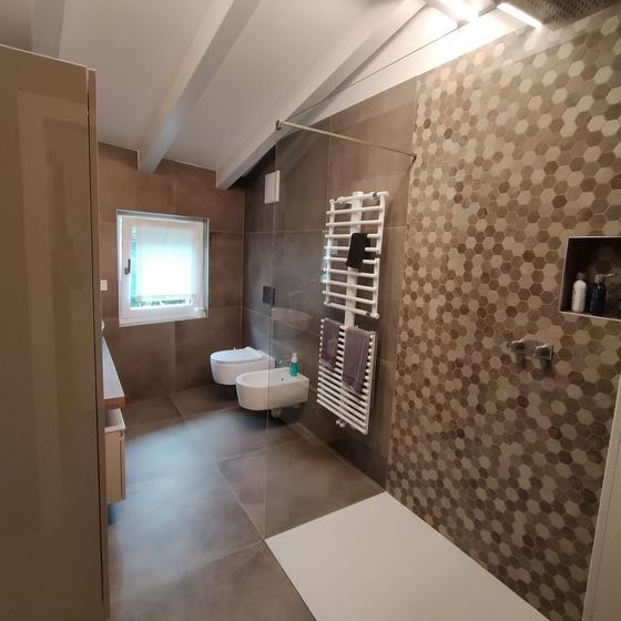 Zona doccia rivestita con mosaico esagonale nei toni della sabbia, accanto a una parete in gres effetto cemento