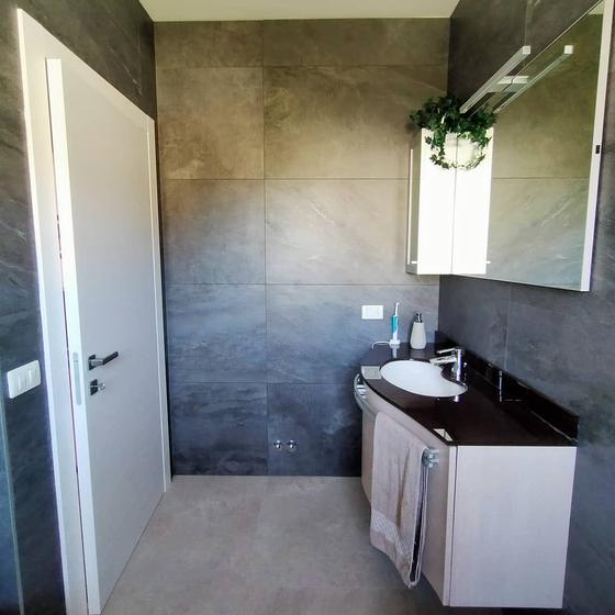 Bagno con grandi lastre a parete bronzo e antracite, pavimento grigio e mobile sospeso con top scuro