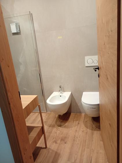 Bagno con pavimento effetto rovere, rivestimento in gres chiaro, sanitari sospesi e mobile in legno