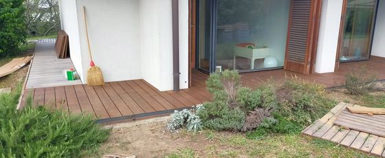 Angolo del porticato con il decking che gira attorno al pilastro e si raccorda con l'aiuola di piante aromatiche