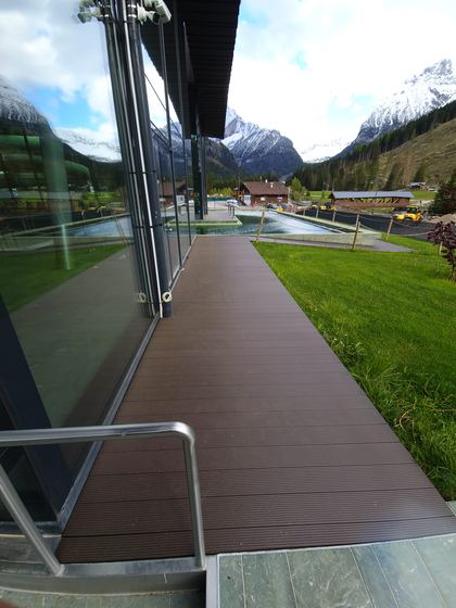 Camminamento in decking posato lungo la vetrata, con il corrimano metallico in primo piano e lo specchio d'acqua sul fondo