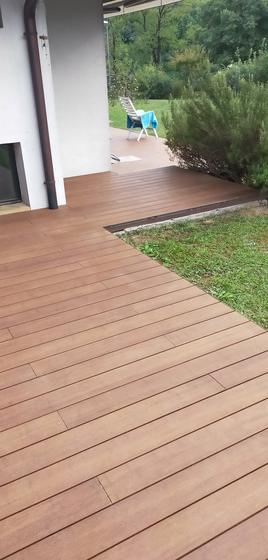 Terrazza con decking a doghe che dal porticato scende fino al bordo del prato, con taglio netto sul verde