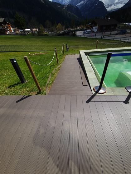 Decking posato attorno alla vasca, con il camminamento che si stacca verso il prato e il bordo in pietra dell'acqua a destra