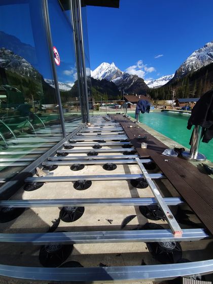 Sottostruttura su supporti regolabili davanti alla vetrata e fascia di decking già posata lungo la vasca, con le cime innevate sul fondo