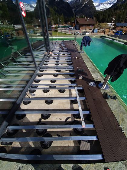 Vista d'insieme del cantiere lungo la vasca, con la sottostruttura a ridosso del parapetto vetrato e la fascia di decking già posata