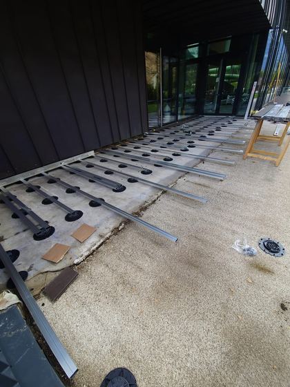 Supporti regolabili e travetti metallici disposti lungo la facciata vetrata, con il materiale su cavalletti in fondo al cantiere