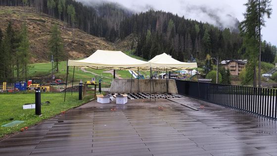Ampia superficie di decking posata e bagnata dalla pioggia, con due gazebo montati sopra e il tratto di fondo ancora da chiudere