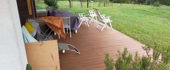 Terrazza in decking sotto il porticato, con tavolo, sedie e lettino da giardino disposti sulle doghe