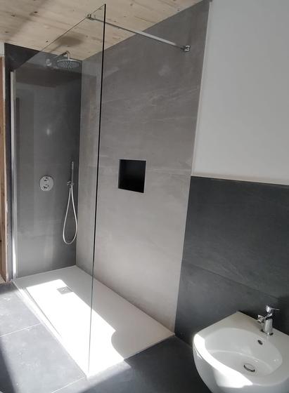 Doccia walk-in con vetro fisso, parete in grandi lastre grigie venate, nicchia nera, pavimento scuro grande formato