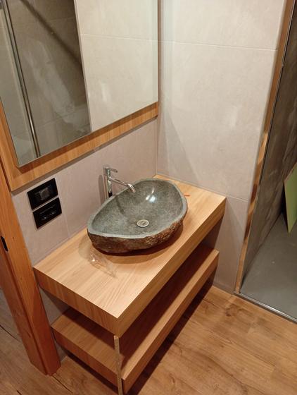 Lavabo in pietra appoggiato su un top in rovere con mensola, specchio incorniciato in legno e pavimento effetto legno