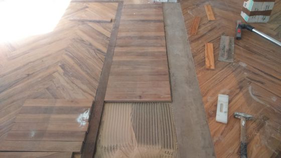Listelli in legno reintegrati dentro un pavimento a spina di pesce, con la colla stesa a pettine, il martello e la spatola appoggiati sul piano