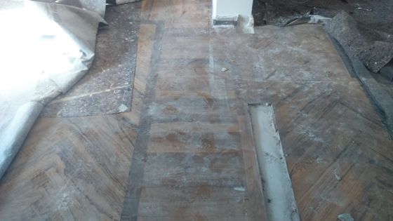 Vecchio pavimento in legno prima dell'intervento, opaco e coperto di polvere, con teli di cantiere arrotolati sul bordo