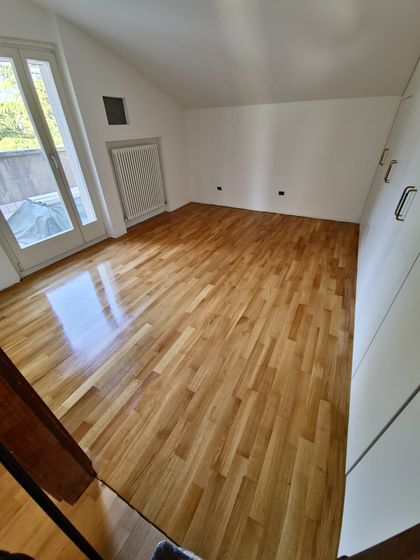 Stanza mansardata con pavimento in legno a listoncini rifinito e lucido, radiatore e portafinestra sul terrazzo