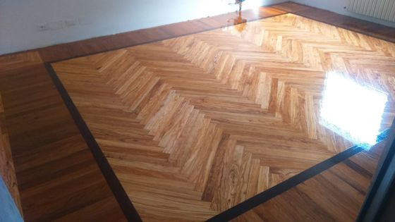 Pavimento in legno a spina di pesce rifinito e lucido, con fascia perimetrale più scura e il riflesso della finestra sulla superficie