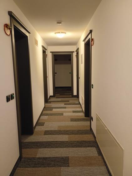 Corridoio di albergo con moquette a doghe nei toni del beige e del grigio, posata in continuità fra le porte