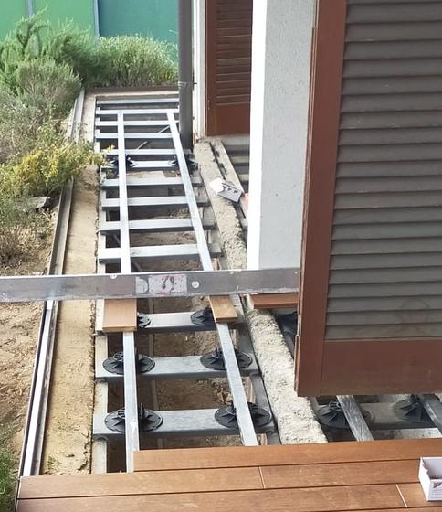 Sottostruttura in profili metallici su supporti regolabili neri accanto alla pavimentazione esterna a doghe già posata